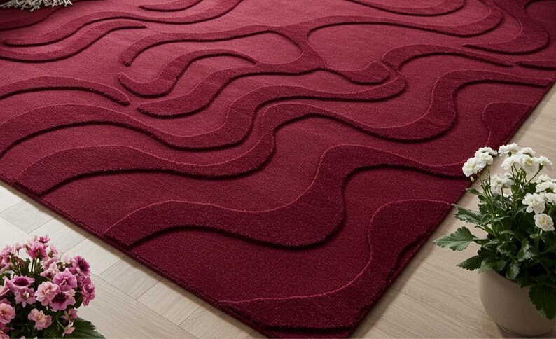 Puede incluir: Una alfombra burdeos con un dise&ntilde;o de ondas. La alfombra tiene una superficie texturizada y un color rojo intenso. El dise&ntilde;o presenta l&iacute;neas onduladas en relieve que crean una sensaci&oacute;n de movimiento y profundidad. La alfombra es de forma rectangular.