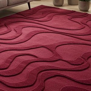 Puede incluir: Una alfombra burdeos con un patr&oacute;n en relieve y fluido. El dise&ntilde;o de la alfombra presenta una serie de formas onduladas interconectadas, creando una superficie texturizada. La alfombra est&aacute; hecha de un material suave y es adecuada para una sala de estar o un dormitorio.