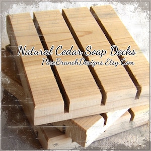 May include: Natural cedar soap decks for holding bars of soap. The decks are made of unfinished wood and have a rustic look. The text "Natural Cedar Soap Decks PineBranchDesigns.Etsy.Com" is printed on the wood.
