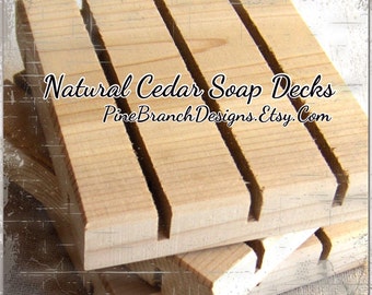 May include: Natural cedar soap decks for holding bars of soap. The decks are made of unfinished wood and have a rustic look. The text "Natural Cedar Soap Decks PineBranchDesigns.Etsy.Com" is printed on the wood.