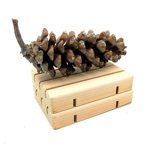 May include: A brown pine cone on a wooden soap dish. The soap dish is made of two pieces of wood stacked on top of each other.