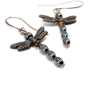 May include: A pair of dangle earrings featuring a dragonfly charm with a copper finish and a row of black hematite beads.