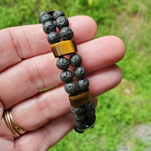 May include: A double-strand bracelet with black lava rock beads and tiger's eye gemstone accents. The bracelet is made of natural materials and has a simple, elegant design.