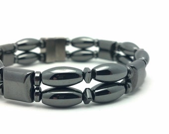 May include: A black hematite bracelet with a magnetic clasp. The bracelet is made of oval-shaped beads and is double-stranded.