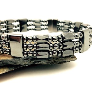 May include: A triple-row bracelet made of black hematite beads and rectangular hematite stones. The bracelet has a magnetic clasp.