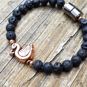 May include: A black lava rock bracelet with a copper bird charm and a magnetic clasp.