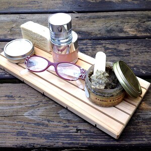 May include: A wooden tray with a small jar of orange and cedar scrub, a small container of lotion, a bar of soap, a pair of red glasses, and a small container of lotion.