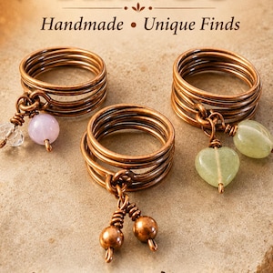 May include: Three copper wire rings with multi-strand bands. One ring features a clear faceted bead and a light purple round bead. Another ring has two light green heart-shaped stones. The third ring includes two small copper spheres.
