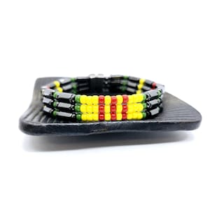 May include: A black, green, and yellow beaded bracelet with a magnetic clasp. The bracelet has three rows of beads, with the middle row being red.