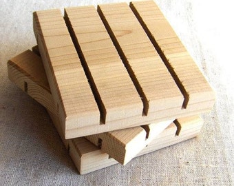 May include: Stacked wooden soap dishes. Each dish is rectangular with parallel grooves cut across the top. The wood has a light, natural color. The dishes are stacked at an angle, showing the side profile.