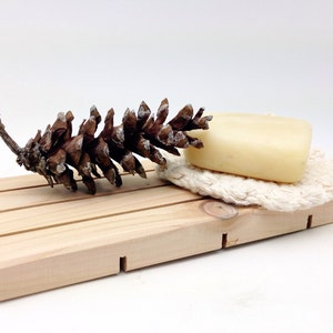 May include: A wooden soap dish with a pine cone and a bar of soap on a white crocheted soap saver.