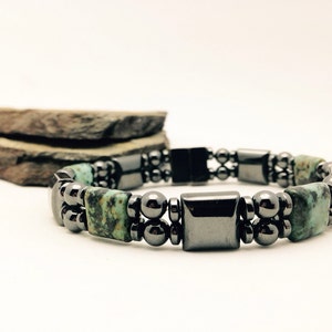 Könnte beinhalten: Ein zweireihiges Armband mit abwechselnden dunkelgrauen Metallperlen und rechteckigen türkis-farbenen Steinperlen mit schwarzer Maserung. Das Design umfasst glatte, polierte kugelförmige Perlen und flache quadratische Perlen in dunkler Metalloptik.