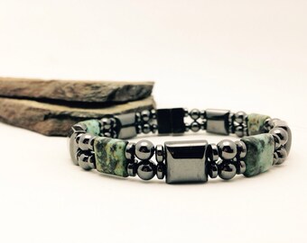 May include: A double-strand bracelet featuring alternating dark gray metallic beads and rectangular turquoise-colored stone beads with black veining. The design includes smooth, polished spherical beads and flat-faced square beads in a dark metallic finish.