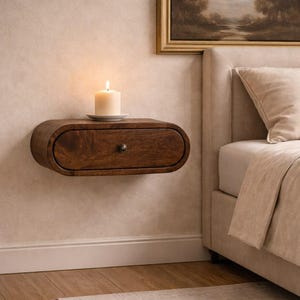 May include: A floating, oval-shaped wooden nightstand with a drawer and a small, round knob. A lit candle sits on top of the nightstand. The nightstand is mounted on a textured wall, near a bed with a beige headboard.