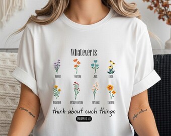 Könnte beinhalten: Weißes T-Shirt mit floralem Design und dem Text "Whatever is...think about such things" in Schwarz. Das Shirt zeigt verschiedene Blumenillustrationen und den Text "Philipper 4,8".