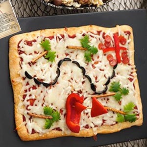 Pode incluir: Uma pizza retangular decorada como um mapa do tesouro pirata. A pizza é coberta com queijo, pimentões vermelhos, azeitonas e palitos de pretzel, dispostos para se assemelhar a um mapa. Uma pequena ilustração do mapa está no canto superior esquerdo.