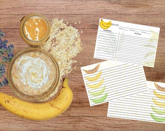 Pode incluir: Uma natureza morta com uma banana madura, uma tigela de aveia e um frasco de mel. Cartões de receitas com ilustrações de banana também estão presentes. A cena é montada em uma superfície de madeira, com raminhos de lavanda.