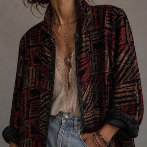 May include: A long-sleeved jacket featuring a black, red, and orange geometric pattern with a button-down front, worn over a cream-colored lace-trimmed camisole and light blue denim jeans, accessorized with layered gold necklaces and bracelets.