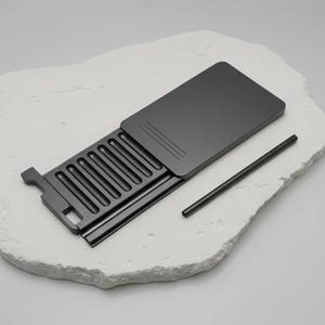 May include: A dark gray metal container with a sliding lid and a matching straw. The container has a series of parallel grooves inside. The lid has three parallel lines etched on it. The items are on a white, textured surface.