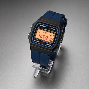 May include: A black Casio F-91W digital watch with a blue strap. The watch face shows the time, date, and day in orange. The watch is water resistant and has alarm and chronograph functions. The strap is made of rubber.