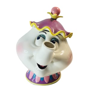 May include: A white ceramic teapot with a smiling face, featuring a purple lid with yellow trim and a pink accent. The teapot has a spout, a handle, and a decorative base with pink and blue accents. The teapot is a character from a popular animated film.