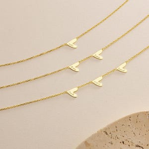 May include: Gold-colored necklaces with heart-shaped pendants. Each heart pendant has a name or date engraved on it. The necklaces are displayed on a light-colored surface.
