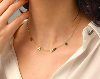 May include: A gold-toned chain necklace featuring the letters M, A, M, and A spaced out along the delicate metal links. The letters are capitalized and integrated directly into the chain, creating a simple, clean, and minimalist jewelry piece.