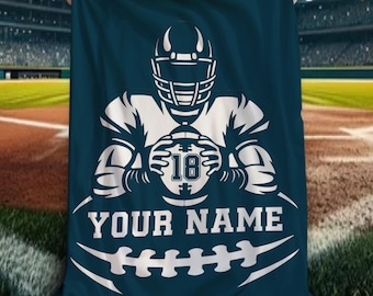 May include: A dark blue rectangular blanket featuring a white graphic of a football player wearing a helmet and holding a football marked with the number 18. Below the player, the text reads YOUR NAME above a stylized white football graphic.