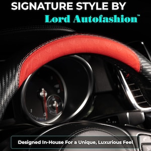 May include: Black and red steering wheel cover with the text "SIGNATURE STYLE BY Lord Autofashion". The cover has a carbon fiber design with a red top section. The text "Designed In-House For a Unique, Luxurious Feel" is also visible.