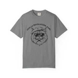 May include: Gray t-shirt featuring a black and white illustration of a cat wearing sunglasses and a beret. The text "VIVA LA REVOLUCIÓN, CARL" is printed above the cat's head. The shirt is a casual style.