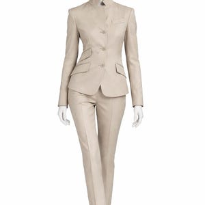 May include: A beige suit displayed on a mannequin. The suit includes a tailored jacket with a mandarin collar, two front pockets, and a three-button closure. The matching pants are straight-legged. The suit is a neutral color, suitable for various occasions.