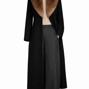 Peut inclure: Un long manteau noir avec un col en fourrure marron, associé à un pantalon large gris. Le manteau est boutonné et présente un design classique. La tenue est présentée sur un mannequin sur fond blanc.