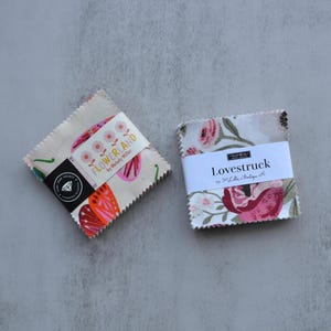 Peut inclure: Deux paquets de tissu avec des motifs floraux. L'un est étiqueté "FLOWERLAND" avec un motif de papillon. L'autre est étiqueté "LOVESTRUCK" avec un motif de rose. Les deux paquets sont carrés et ont une bande blanche.