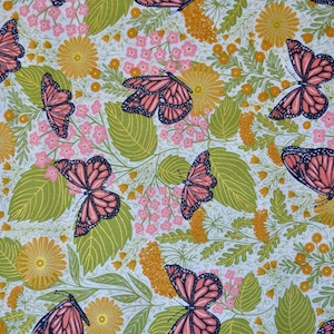 May include: A fabric pattern featuring monarch butterflies with orange and black wings, set against a backdrop of green leaves, yellow flowers, and pink blossoms. The design is on a white background.