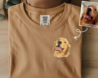 May include: A tan t-shirt with a pocket-sized illustration of a Golden Retriever dog. The shirt has a crew neck and a tag that reads "Comfort Colors". A small photo of the dog is shown next to the shirt. The words "custom name" and "pocket size" are also visible.