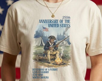 May include: Cream-colored t-shirt featuring a graphic commemorating the 250th anniversary of the United States. The design includes an illustration of a colonial soldier, text that reads "250th Anniversary of the United States", and the text "Descendant of a Patriot, Levis Stansbury, 1758-1818, North Carolina."