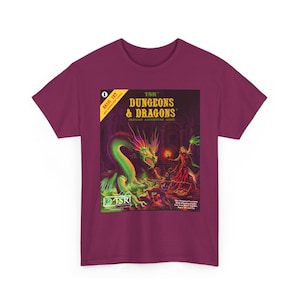 May include: A maroon t-shirt featuring a colorful graphic from the Dungeons & Dragons fantasy adventure game. The graphic includes a green dragon, a sorceress, and the game's logo. The shirt is a basic set.