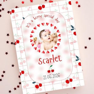 May include: A personalized greeting card with a baby's photo, surrounded by a heart-shaped frame. The card features a cherry theme with the text "It's a berry special day" and the name "Scarlet" in red. The date "21.06.2026" is also included.