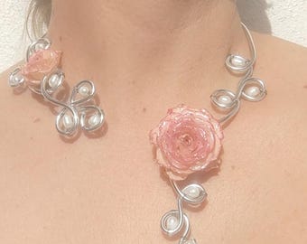 May include: A handcrafted necklace and earring set featuring a silver wire design. The necklace has a large pink rose and a dangling blue crystal. The earrings have a smaller pink rose. Faux pearls are incorporated throughout the design.