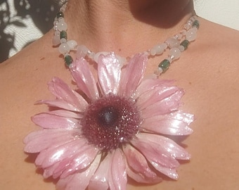 May include: A unique necklace featuring a large, light pink flower pendant with a dark center and a clear teardrop-shaped charm. The necklace has a double strand of beads in white, pink, and green.