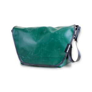 Könnte beinhalten: Grüne Messenger-Tasche mit schwarzem Riemen und Besatz. Die Tasche hat einen Klappverschluss und ein Etikett mit der Aufschrift "sourced!". Sie besteht aus strapazierfähigem Material und ist zum Tragen von Gegenständen konzipiert.