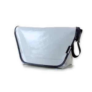 Può includere: Una borsa a tracolla grigio chiaro con finiture e cinturino neri. La borsa ha una forma rettangolare con chiusura a patta. La parola "sourced" è stampata su un'etichetta nera attaccata al cinturino.