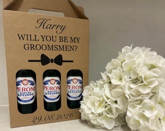 Könnte beinhalten: Eine braune Pappschachtel mit dem Text "Harry WILL YOU BE MY GROOMSMEN?" und drei Peroni Nastro Azzurro Bierflaschen. Das Datum "29.08.2026" ist unten aufgedruckt. Rechts ist ein Strauß weißer Blumen.