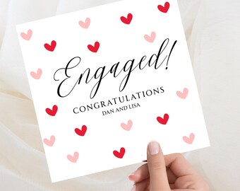 Könnte beinhalten: Eine quadratische, weiße Verlobungskarte mit roten und rosa Herzillustrationen. Das Wort "Engaged!" ist in eleganter schwarzer Schrift geschrieben, darunter "Congratulations Dan and Lisa".