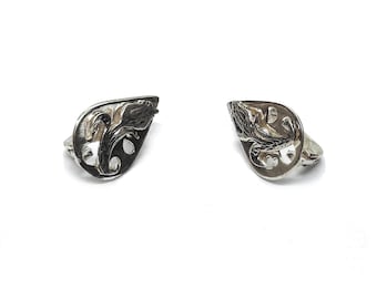 May include: A pair of silver-toned metal earrings featuring a teardrop-shaped silhouette with an intricate, openwork cutout design. The surface displays a polished finish with darkened recessed areas that highlight the swirling, organic patterns.