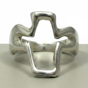 Könnte beinhalten: Ein silberfarbener Ring mit einem offenen, ausgeschnittenen Design, das eine Kreuzform bildet. Das Metall hat eine glatte, polierte Oberfläche mit abgerundeten Kanten und einem durchgehenden Ringband, das mit der zentralen Kreuzstruktur verbunden ist.