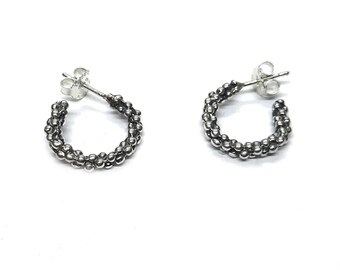 May include: A pair of silver hoop earrings featuring a textured surface composed of numerous small, rounded beads. Each earring is designed as a circular hoop with a post back closure, showcasing a metallic finish with dark oxidized detailing.