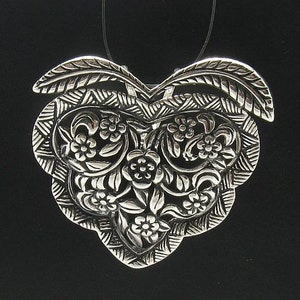 May include: A silver pendant in the shape of a heart with intricate floral designs.