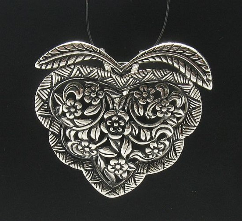May include: A silver pendant in the shape of a heart with intricate floral designs.