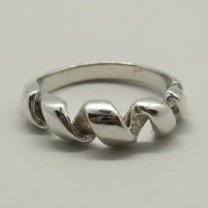 May include: A polished silver-toned ring featuring a continuous, spiralling ribbon-like design that wraps around the band. The metal surface is smooth and reflective, creating a series of interconnected, curved loops that form the circular ring structure.